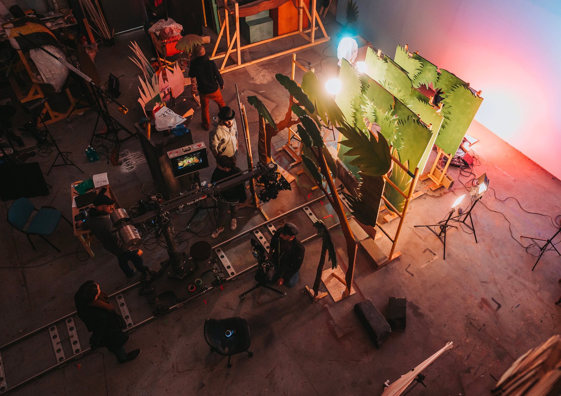 Vue plongeante sur le studio : rails de travelling, grue, moniteur et équipe autour d’une jungle de feuilles en carton peint.