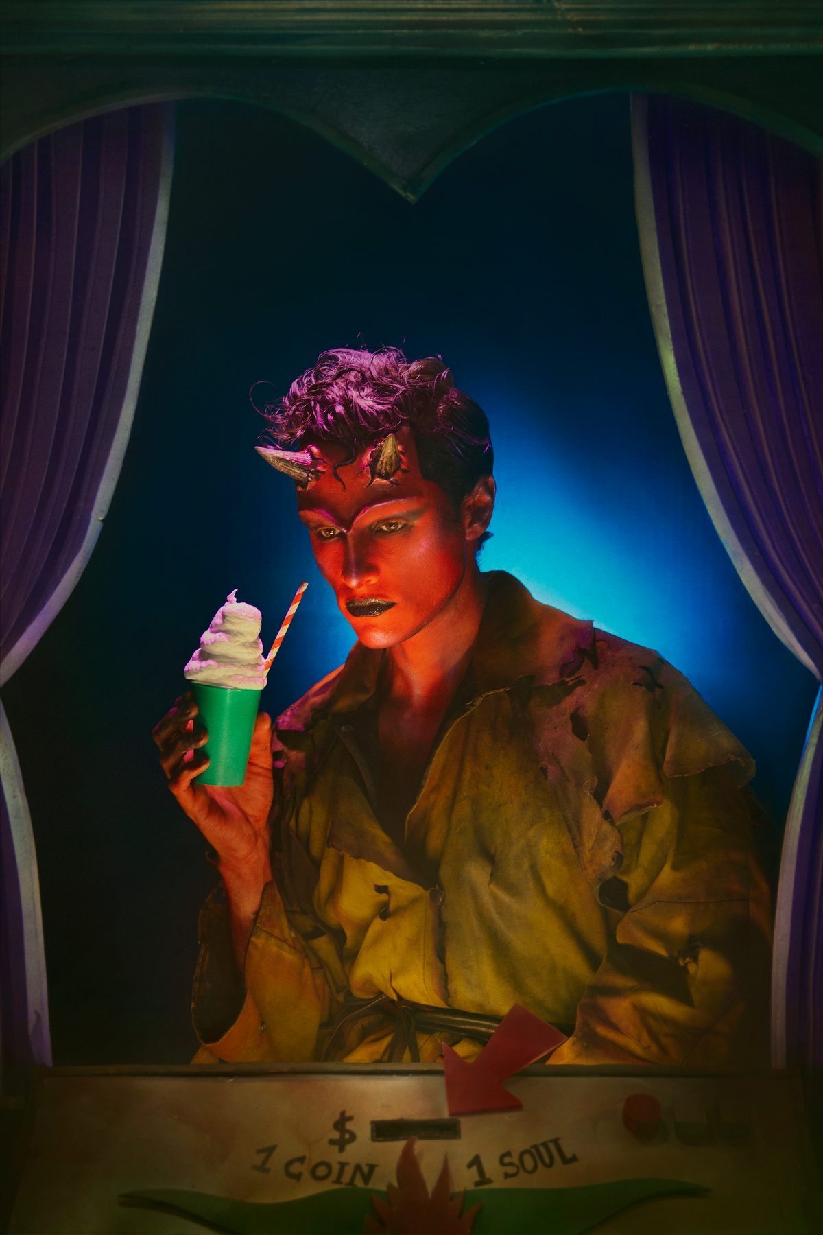 Un diable au visage rouge boit un milk-shake derrière un comptoir où l’on lit « 1 coin, 1 soul ».